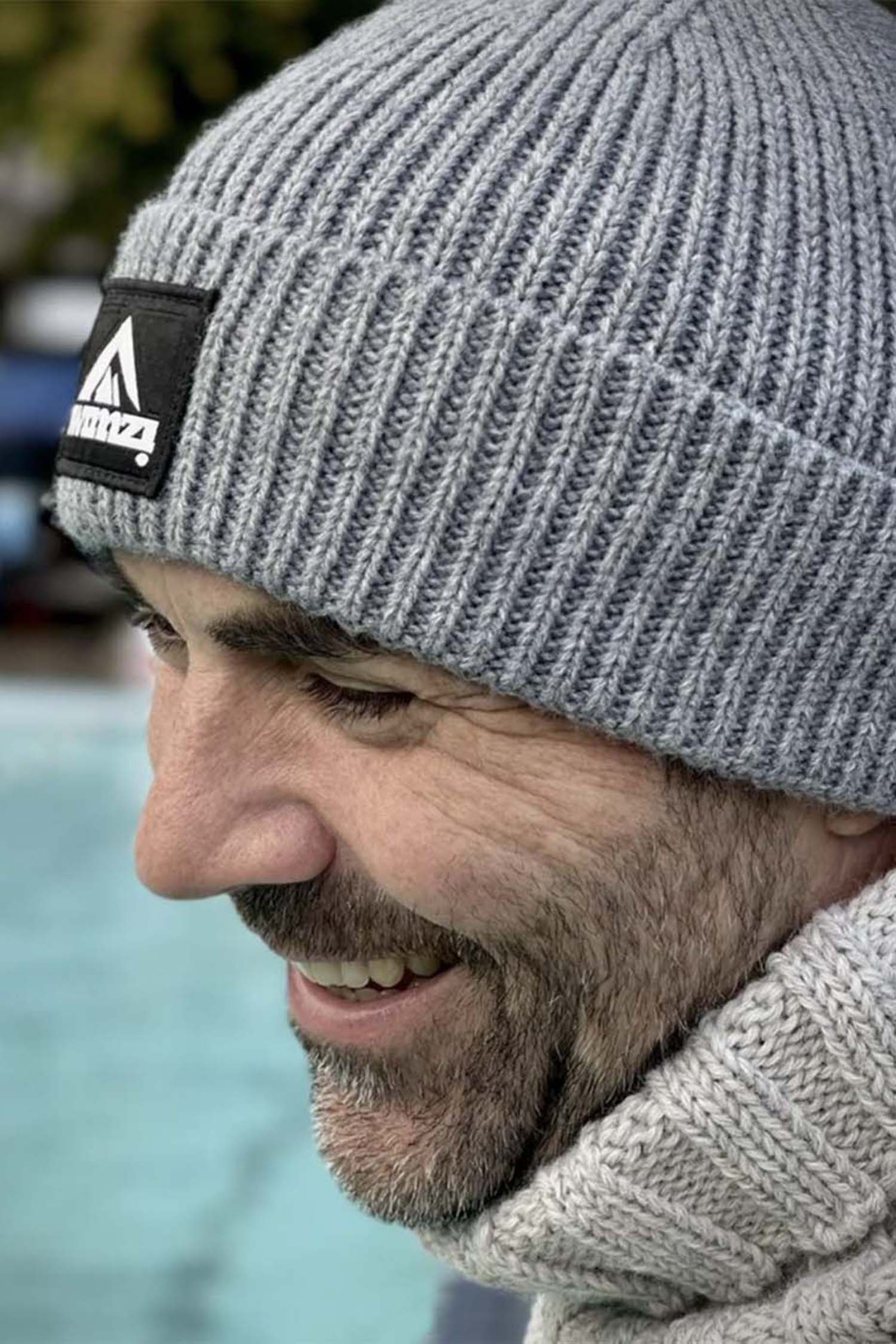 Man wearing a simple beanie hat knitted in a chunky single rib in a silver grey shade. There is a SWIMZI badge sewn to the front of the deep turn back headband.