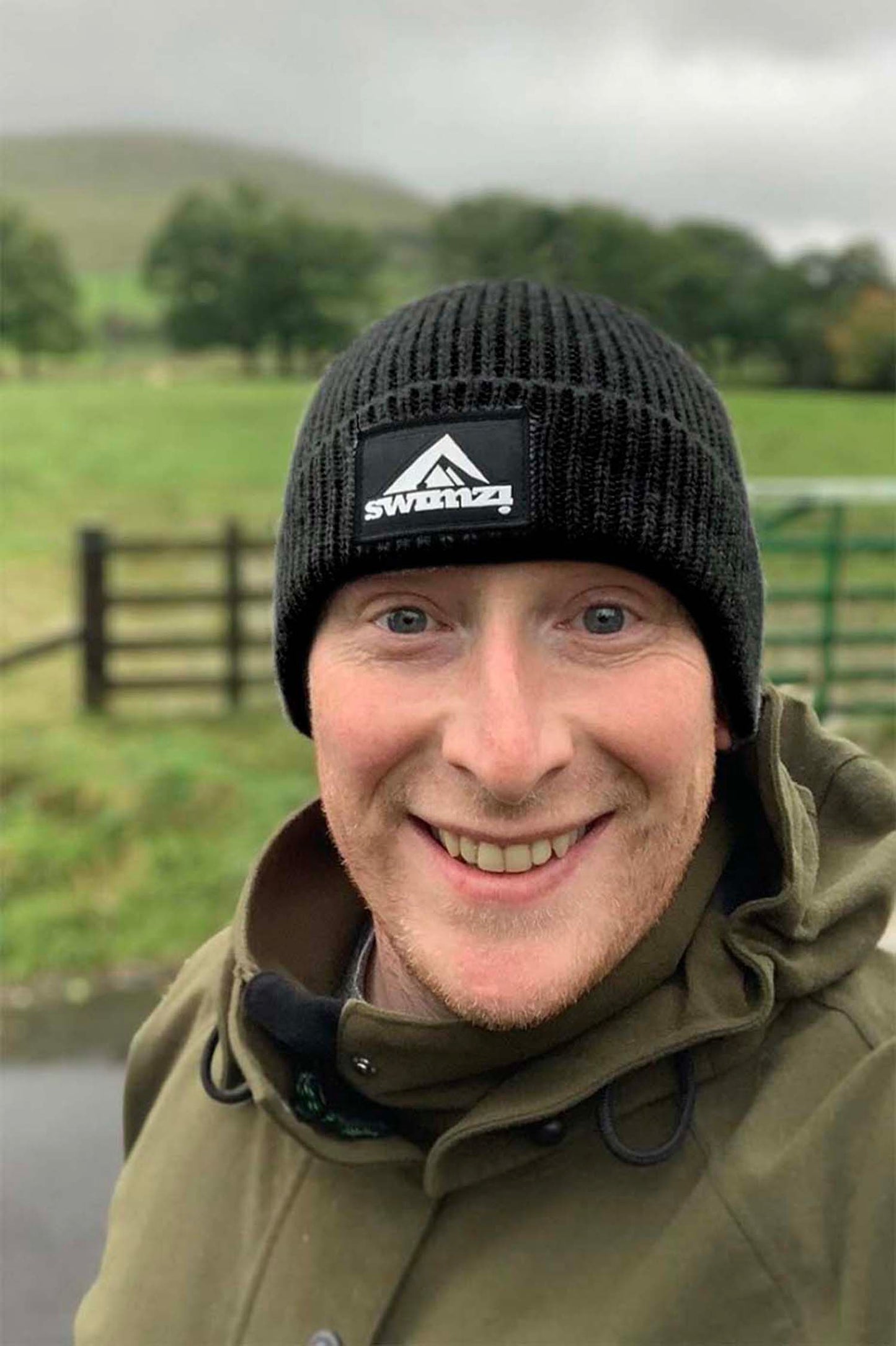 Man wearing a simple beanie hat knitted in a chunky single rib in a jet black shade. There is a SWIMZI badge sewn to the front of the deep turn back headband.